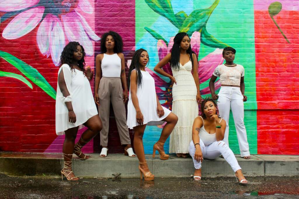 Group of young African women in stylish outfits in front of a colourful mural